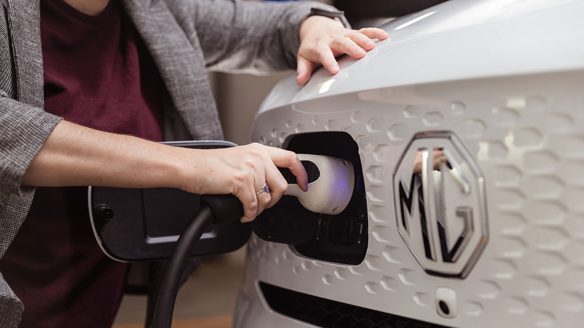 Woman plugging charging socket into port at front of MG ZS EV electric car