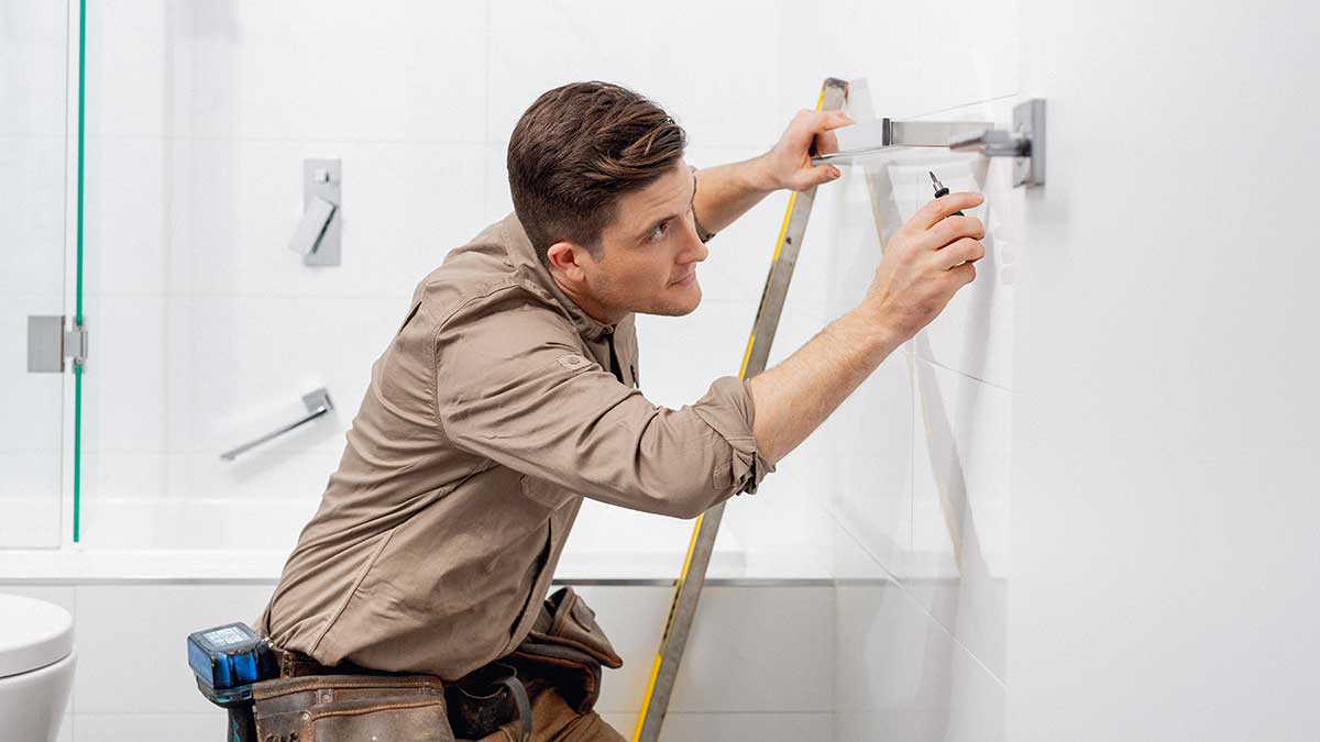 A tradesperson installing a heated towel rail on a bathroom wall