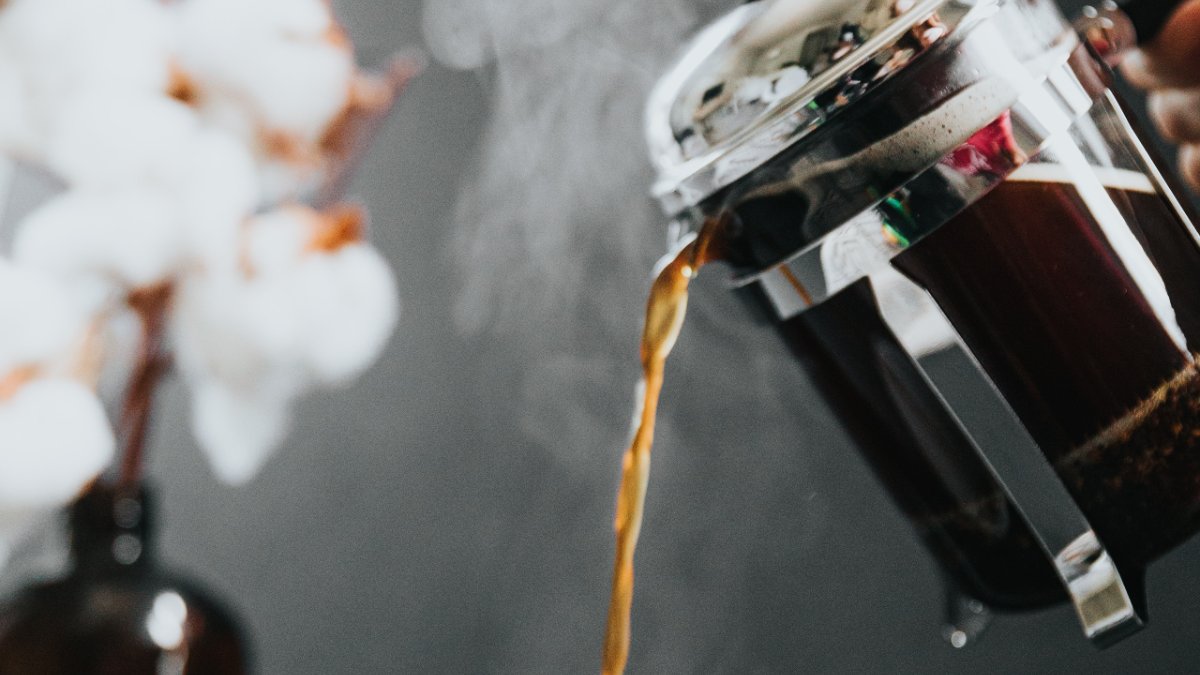 coffee being poured out of a coffee plunger next to white flowers