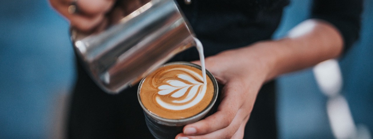 barista pouring frothed milk into a coffee cup