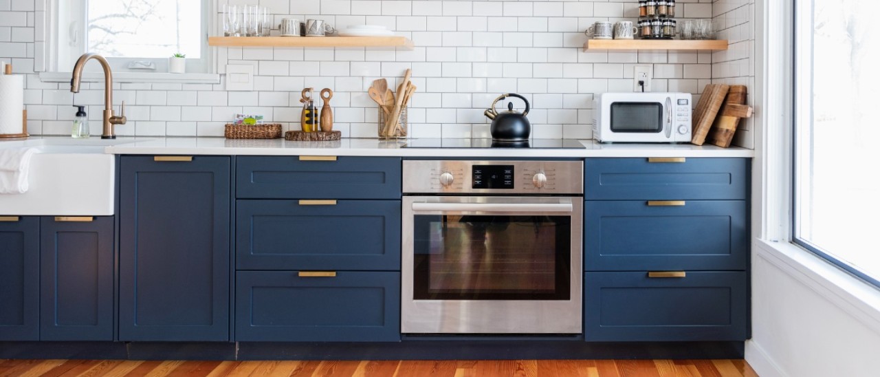 A modern kitchen featuring dark blue cabinetry, white subway tiles and a modern oven with induction cooktop