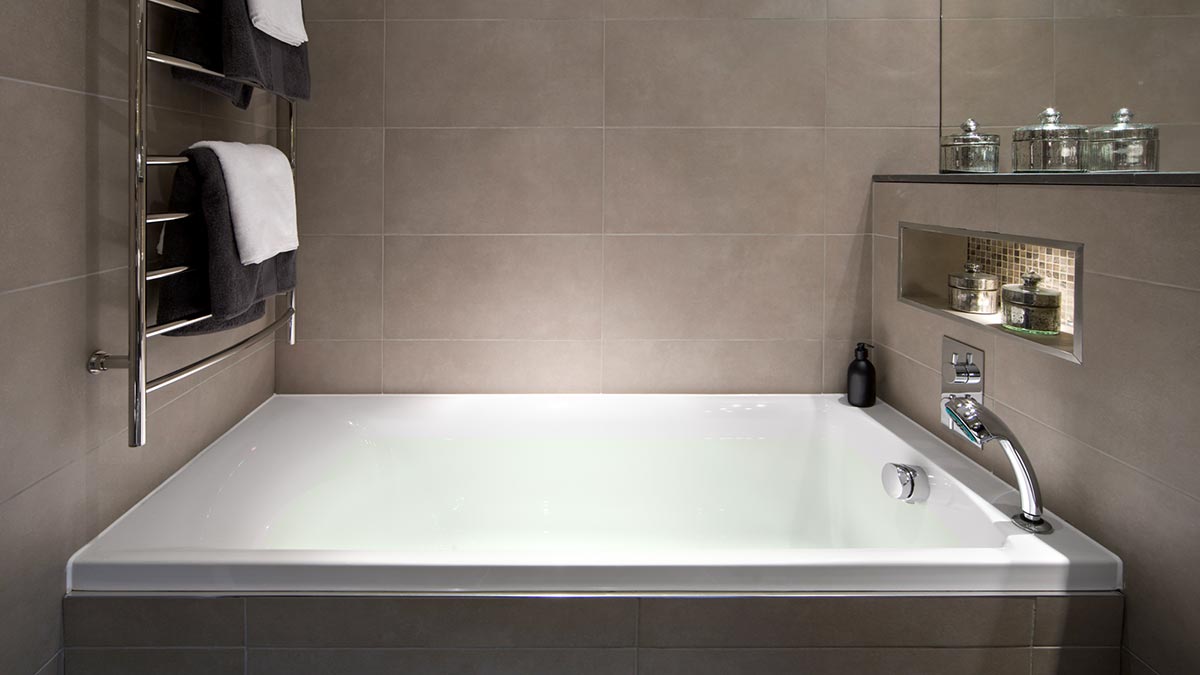 A silver ladder-style heated towel rail installed next to a modern bathtub. 