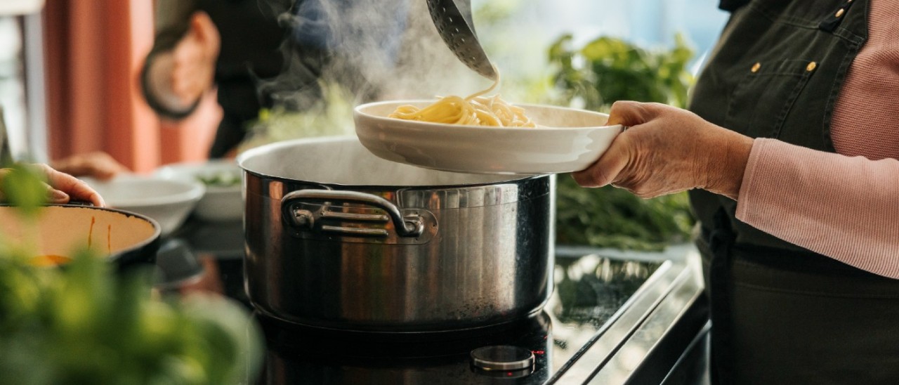 woman lading spaghetti out of pot on induction cooktop
