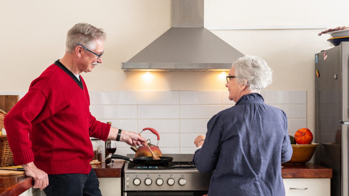 An elderly couple cooking in a modern kitchen with the lights on their stainless steel canopy-style rangehood