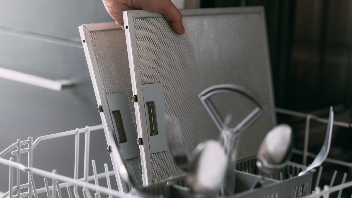 A person putting two metal mesh rangehood filters into a dishwasher