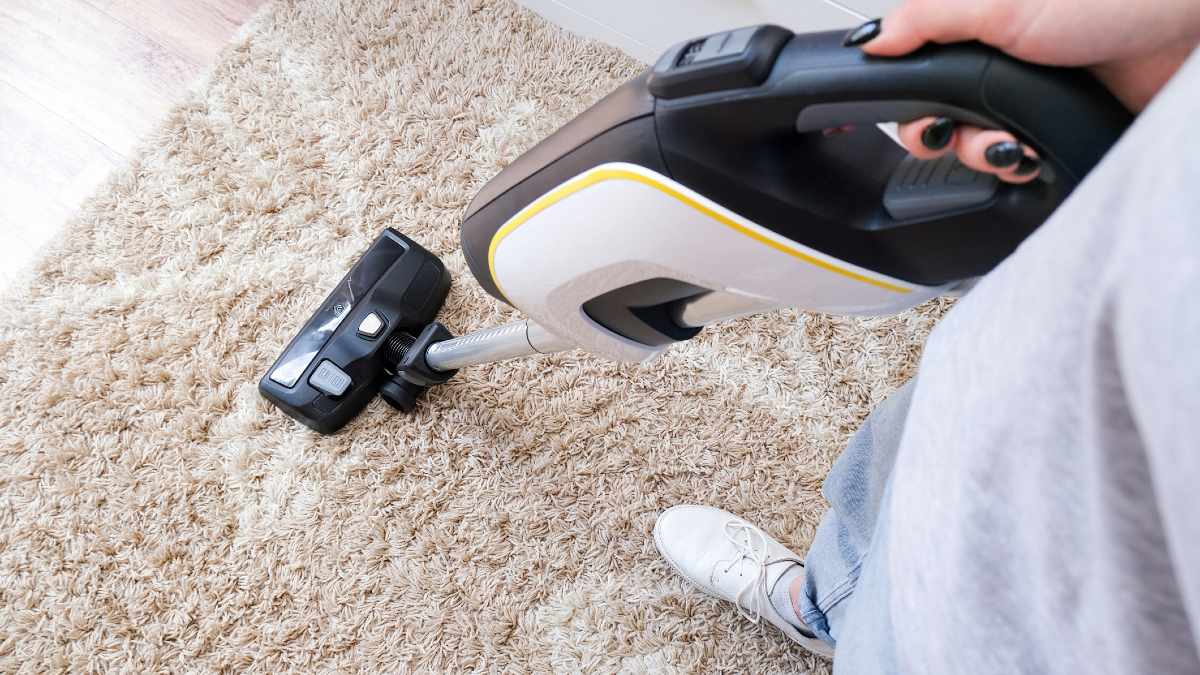 A person vacuuming a white furry rug with a stick vacuum