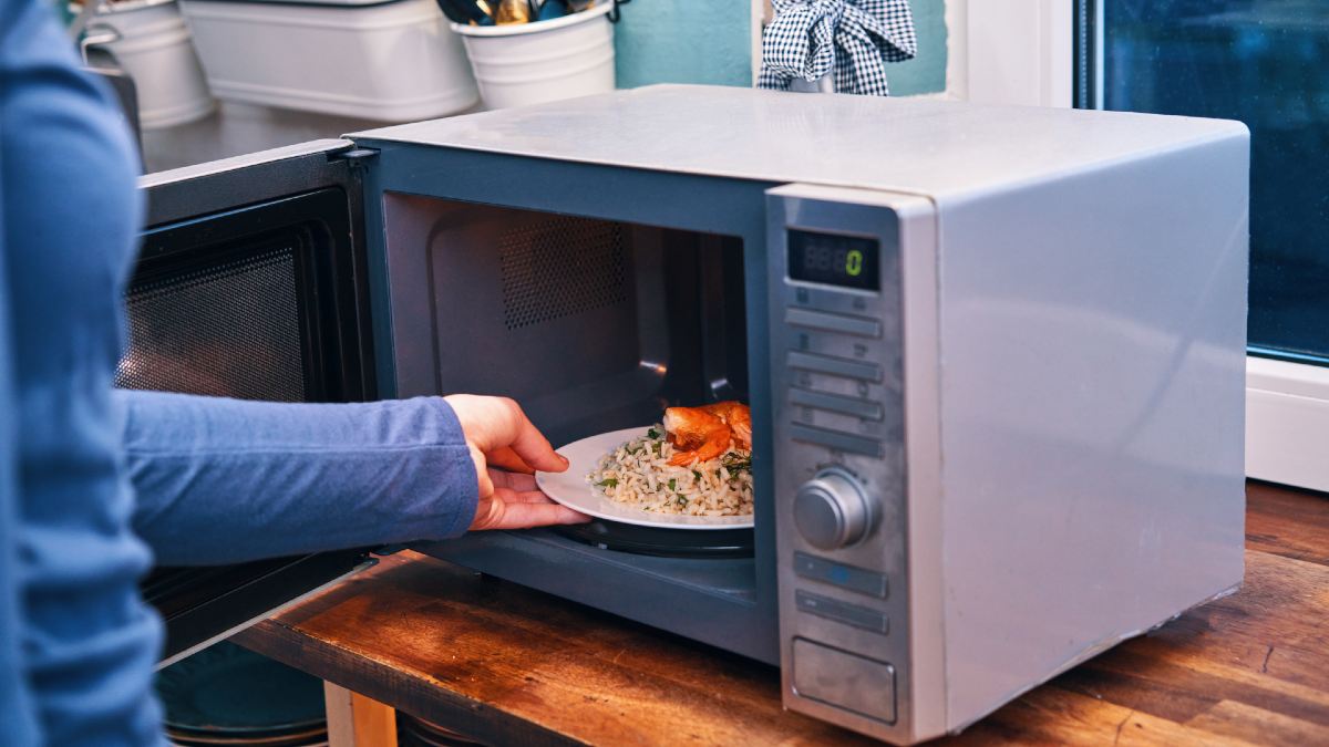 woman placing a plate of food into a microwave