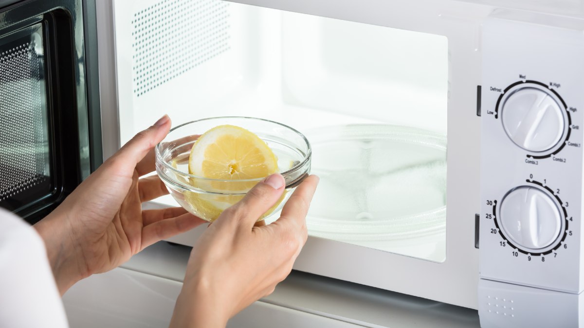 woman placing a microwave-safe bowl with a lemon slice into her microwave for cleaning