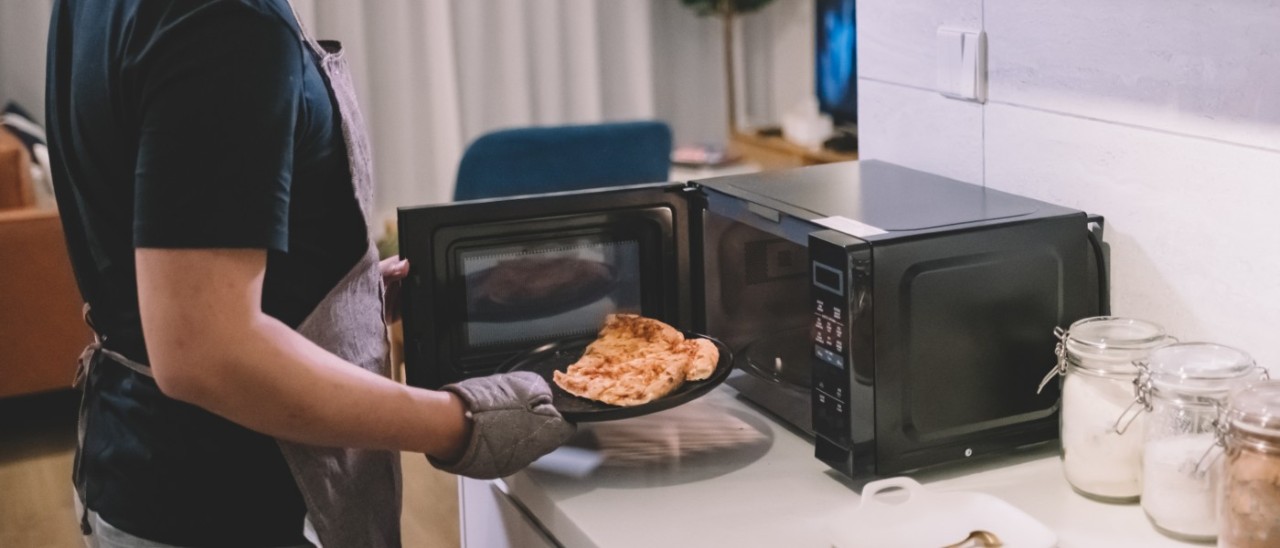 Microwave_Getty young man using oven gloves to take a plate of food out of a microwave