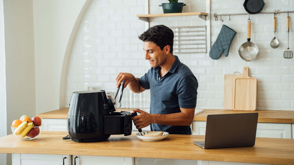busy man cooking with an air fryer beside an open laptop
