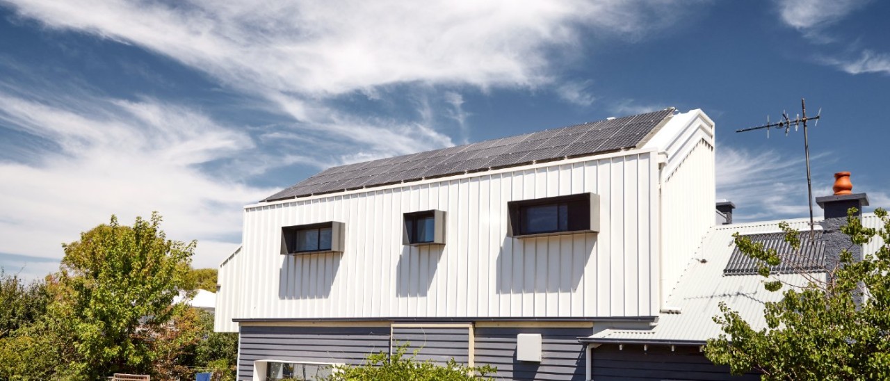 A large number of solar panels installed on a house roof under a lightly cloudy, wintery sky