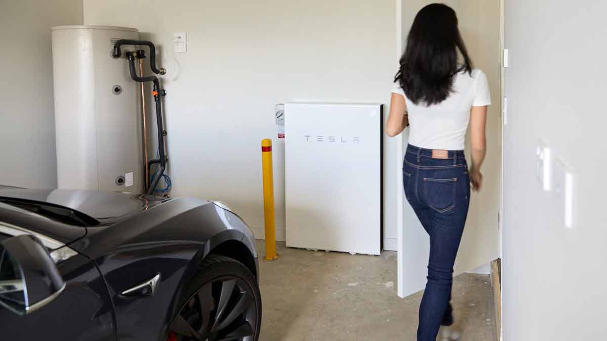 parked Tesla and woman walking into house from garage with Tesla Powerwall solar battery on wall