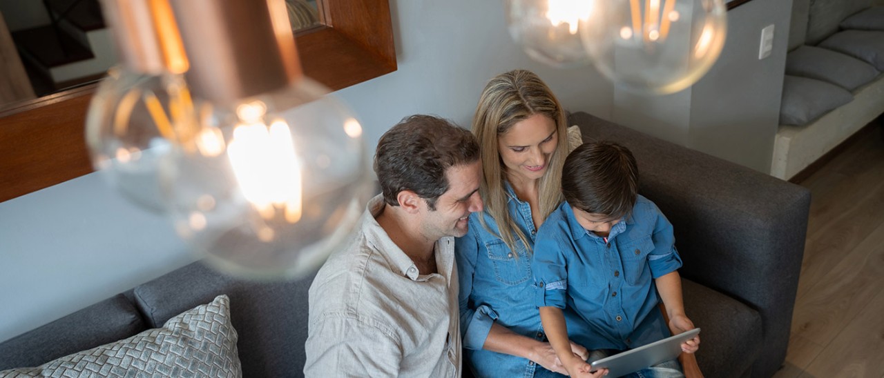 Overhead shot of family on couch looking at tablet with lights in foreground.