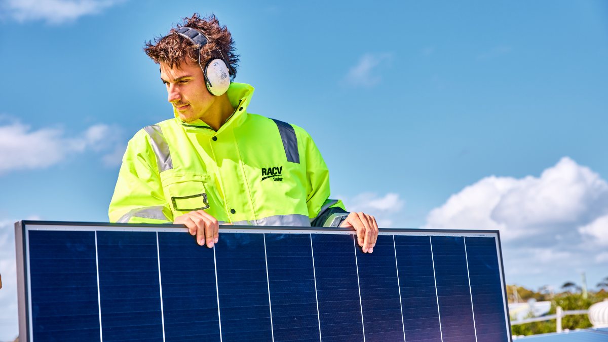 young man in RACV hi-vis jacket holding a solar panel