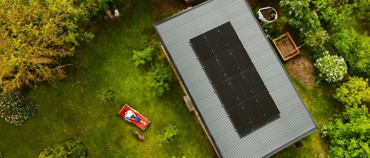 Solar Backyard aerial view of rooftop solar panels with woman and dog lying in backyard