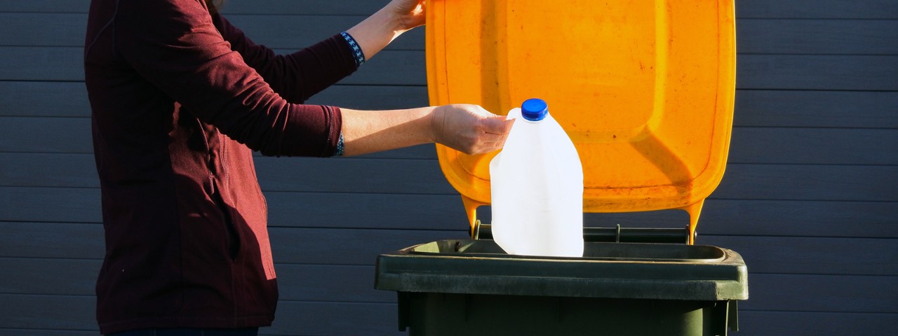 1331199279 A person putting a milk bottle into a recycling bin