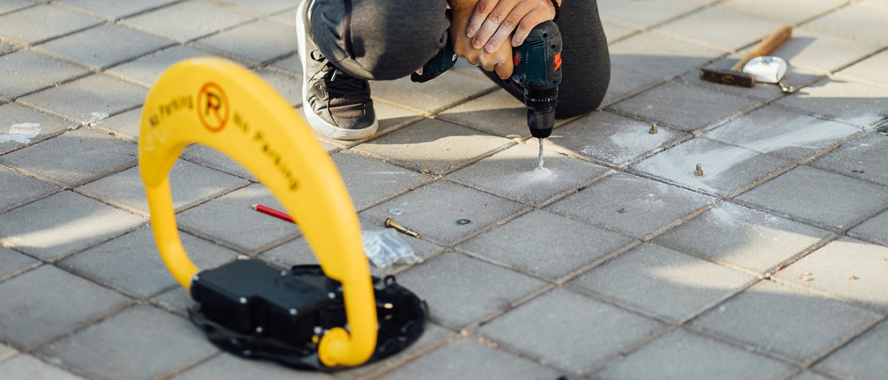 Person drilling hole in concrete tile to install security bollard