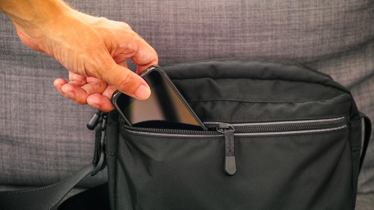 A person putting a smartphone into a black Faraday bag