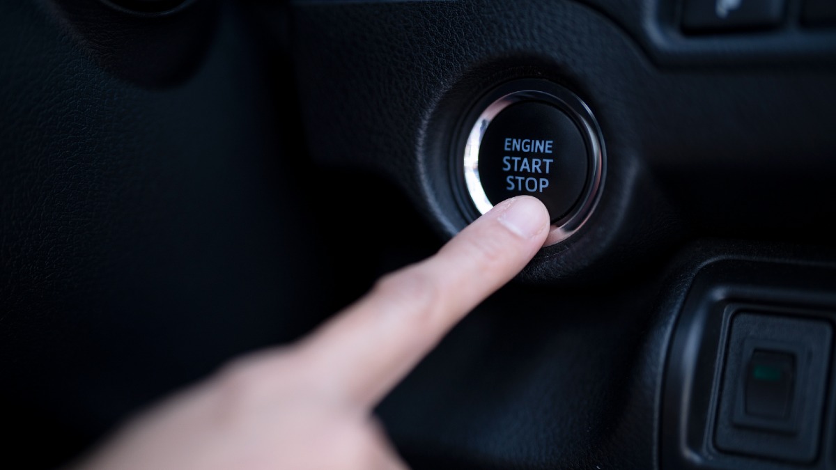 person pushing start button in car
