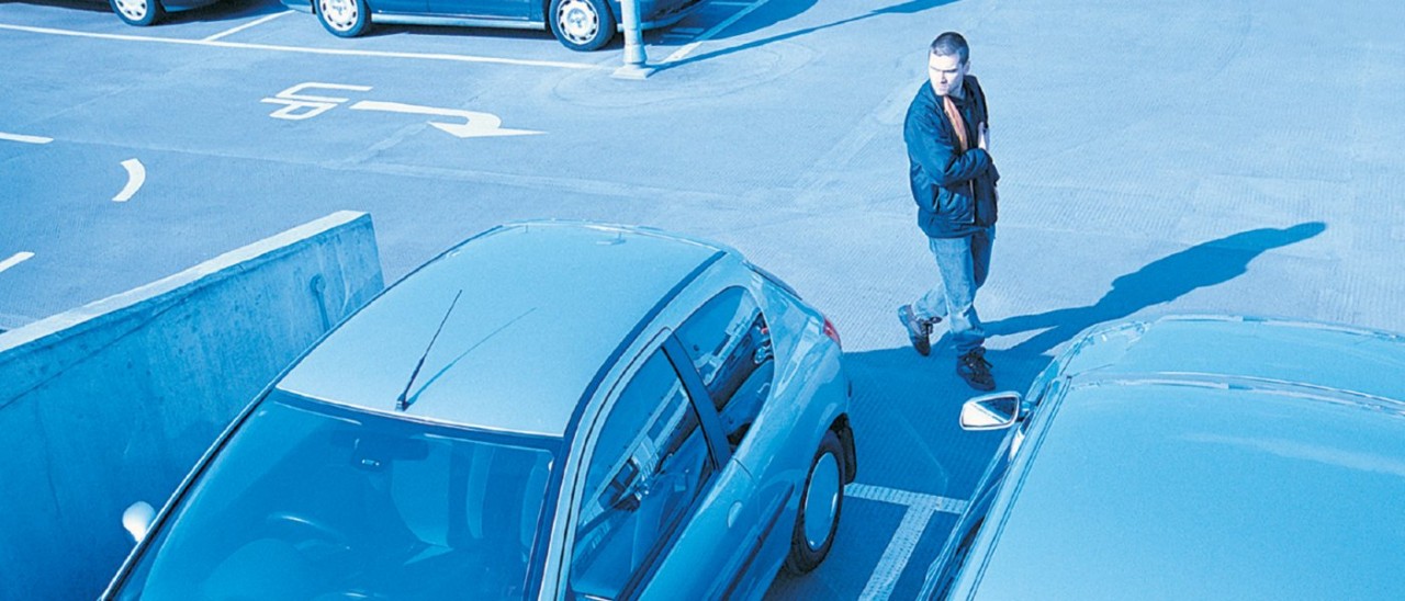 A suspicious man looks at cars as seen on a CCTV camera