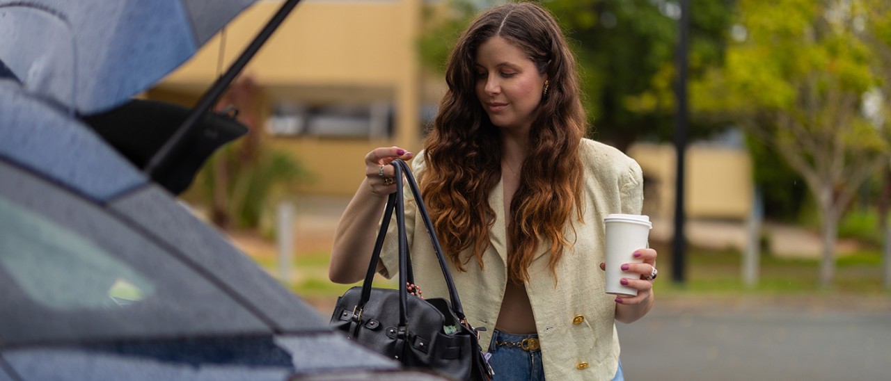 Woman holding coffee and getting bag out of boot.