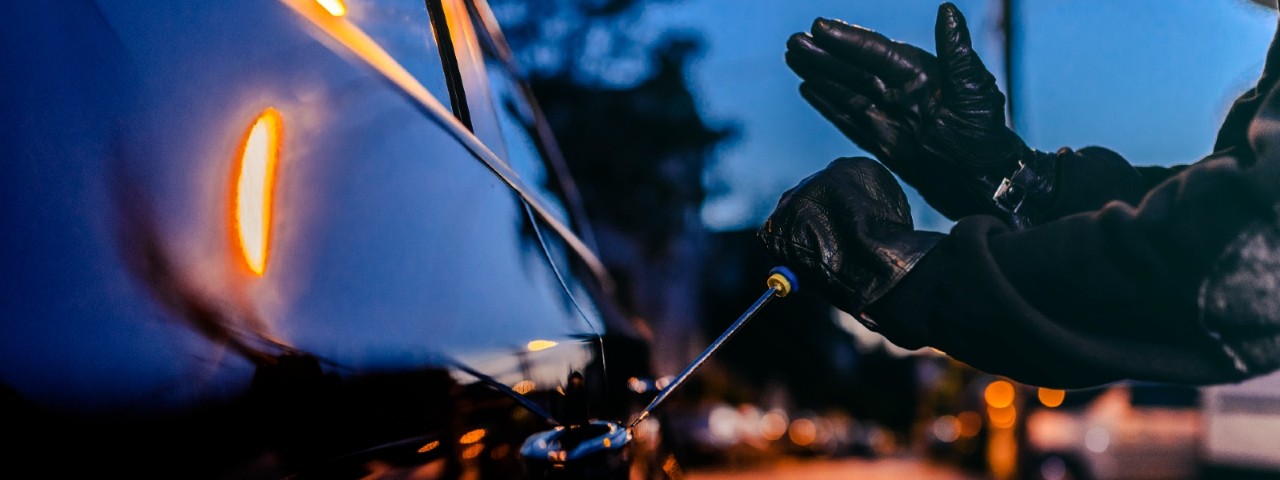 thief breaking into a car with a screwdriver