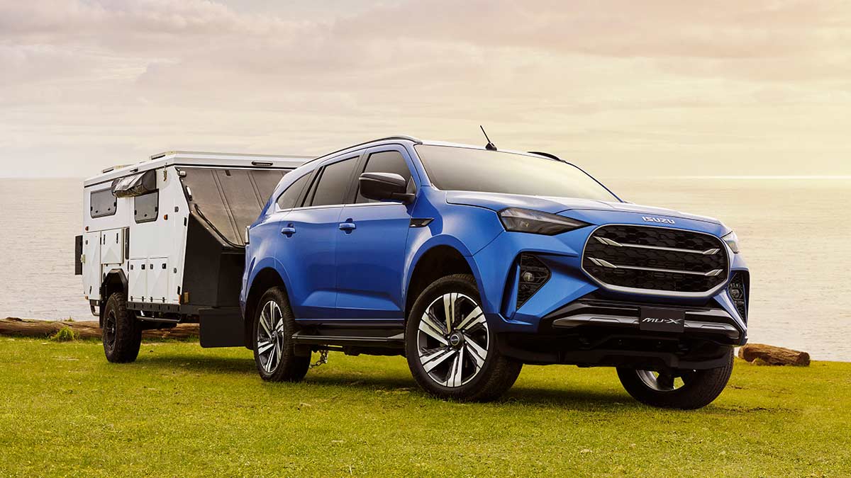 Blue Isuzu MU-X SUV with white caravan on grassy clifftop overlooking ocean.