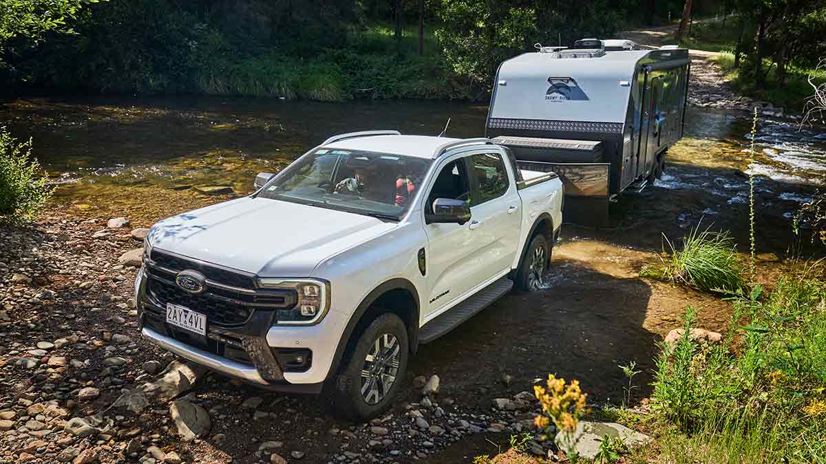 White Ford Ranger Wildtrak ute towing caravan and crossing rocky creek in bush location