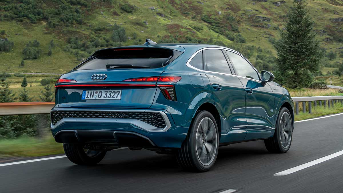 Rear view of blue metallic Audi Q3 small SUV driving on winding road in Scottish Highlands.