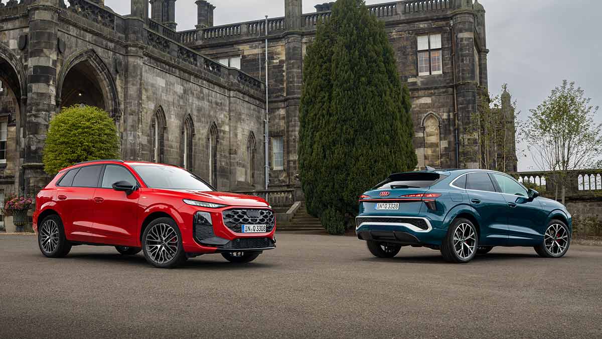 Two Audi Q3 small SUVs, red at front and blue rear, parked in front of grand Scottish heritage building.