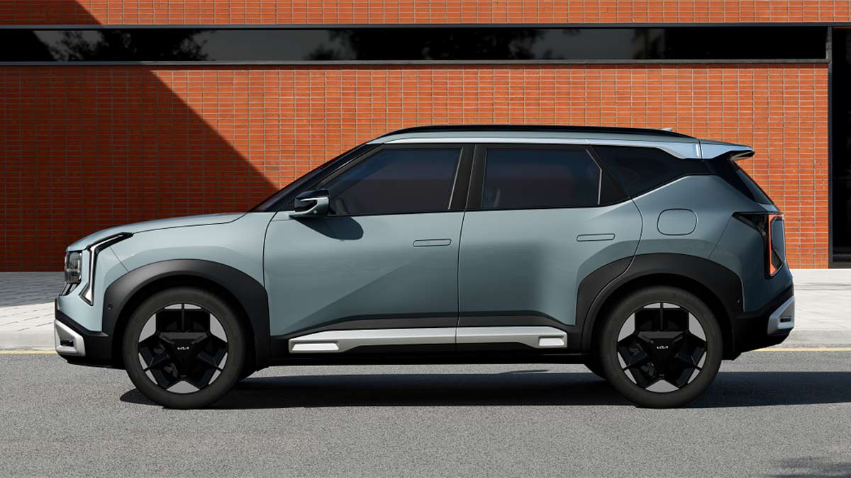 Side view of light blue Kia Seltos small SUV parked in front of red brick building.