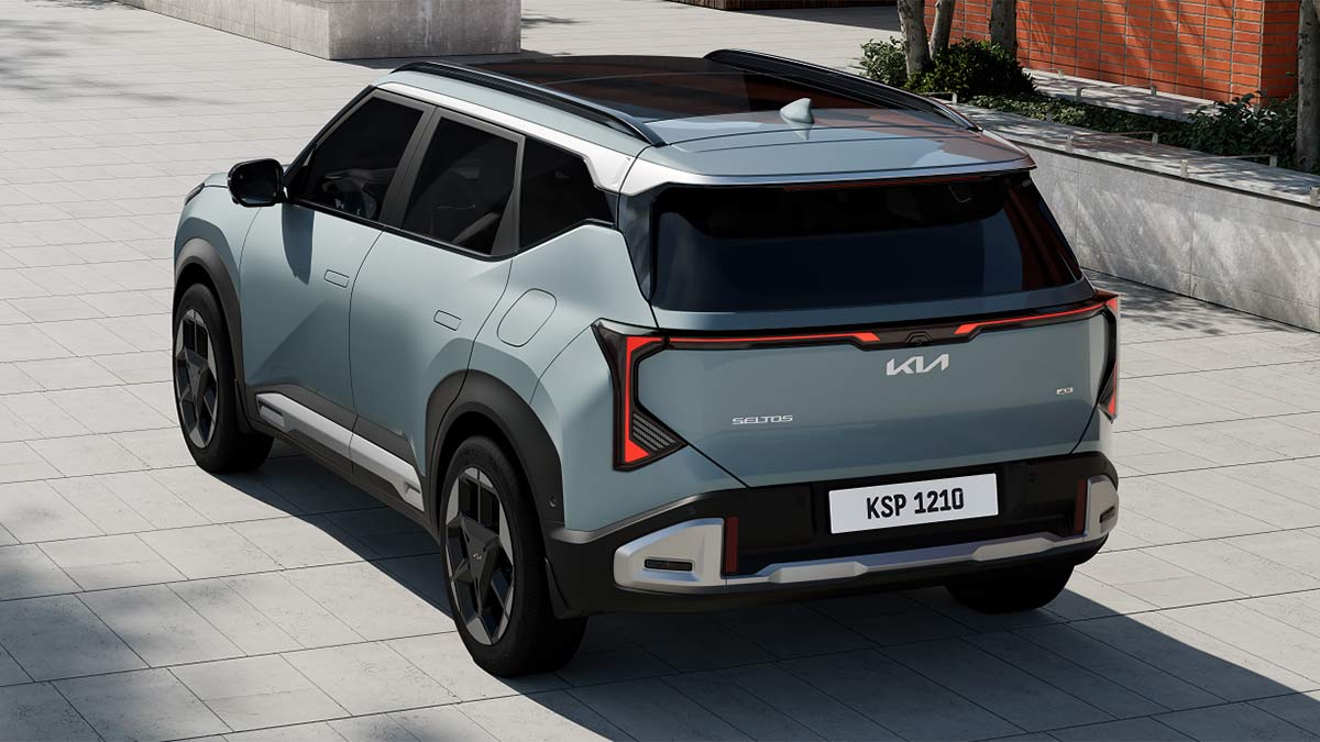 Overhead rear view of light blue Kia Seltos small SUV on street in front of red brick building.