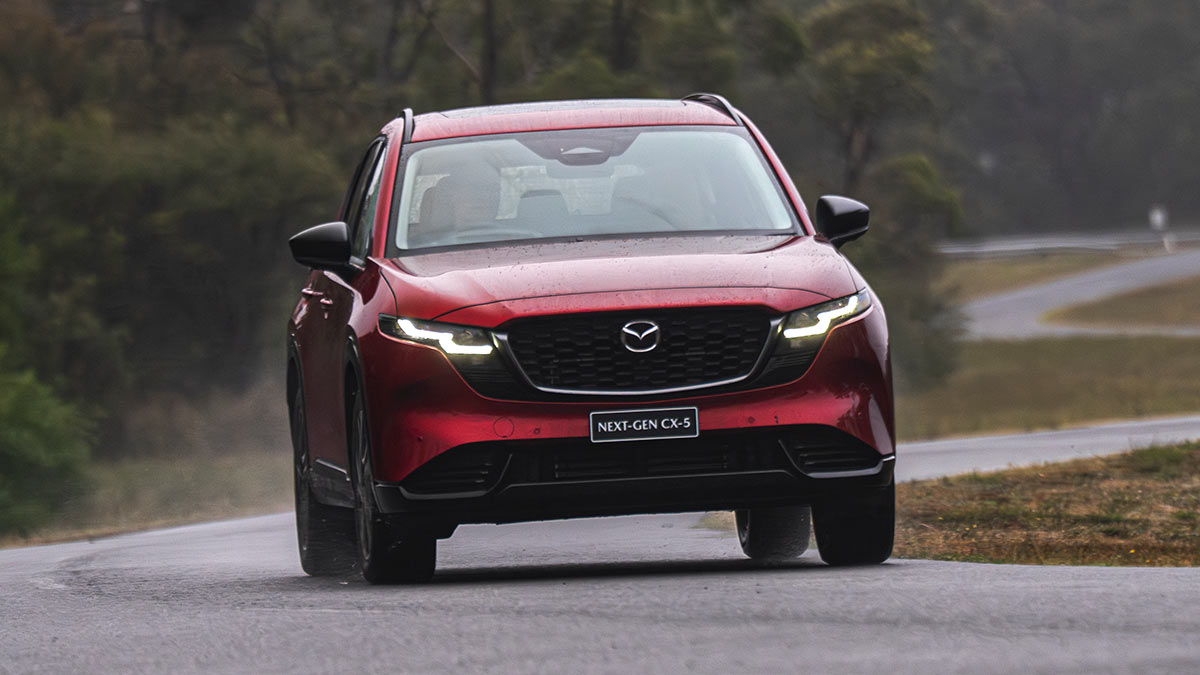 Red Mazda CX-5 SUV driving on twisty wet road at bushy Lang Lang proving ground in Victoria.