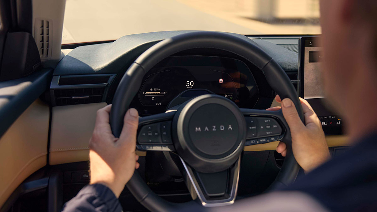 Driving holding steering wheel in Mazda CX-5 with digital instruments showing speed sign limit and other functions.