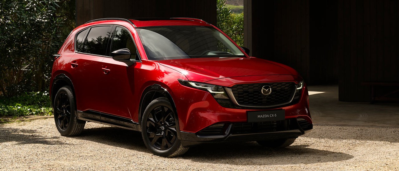 Red Mazda CX-5 medium SUV parked outside dark timber-cladded building.
