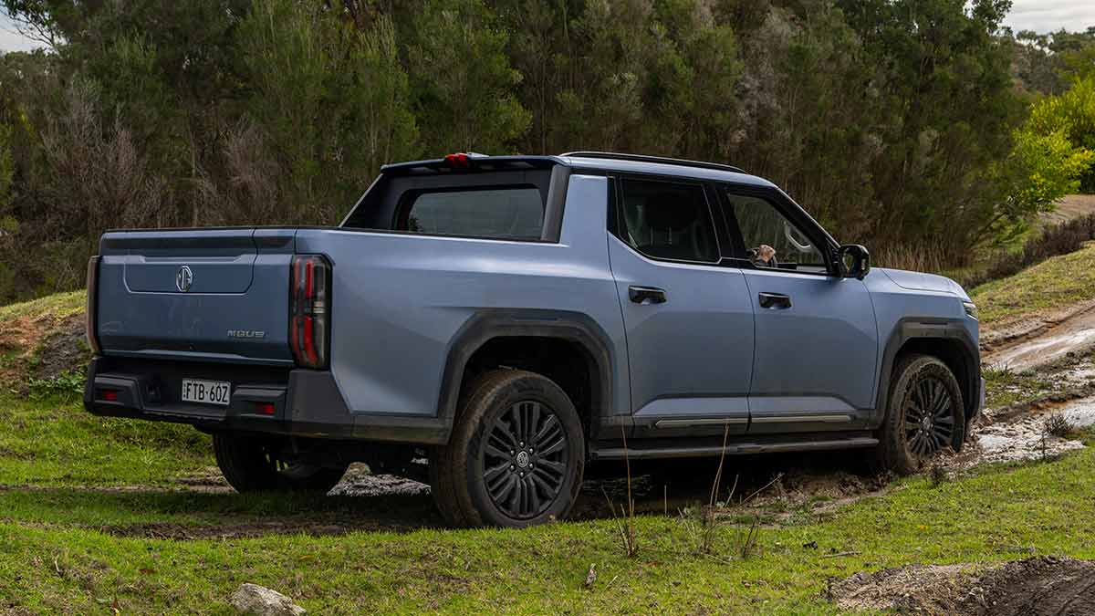 Rear shot of blue MG U9 dual-cab ute at base of muddy incline on off-road course.