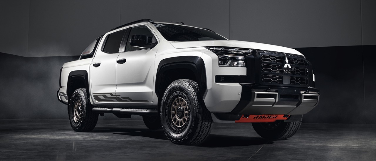 White Mitsubishi Triton Raider dual-cab ute parked on polished concrete floor in empty, dimly lit warehouse.