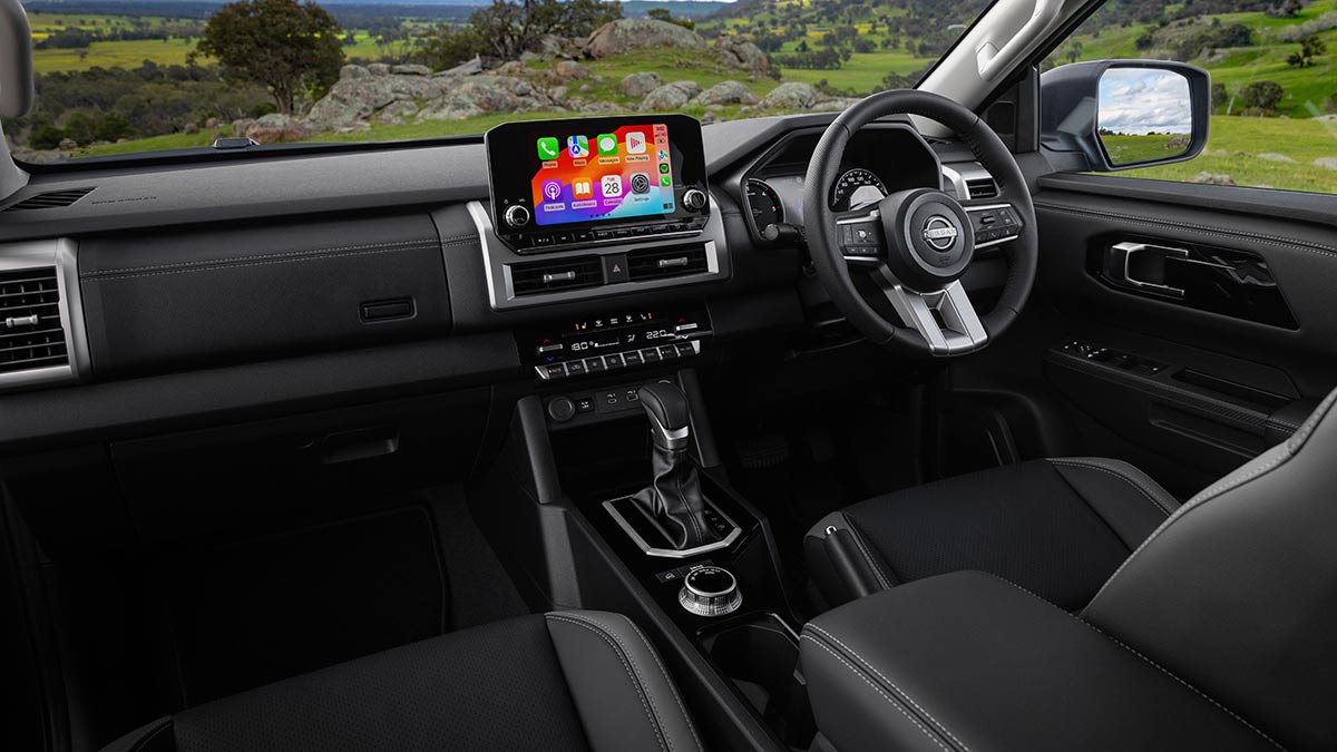 Driver's area of Nissan Navara ST-X with dark grey trim, metallic highlights and large central touchscreen.