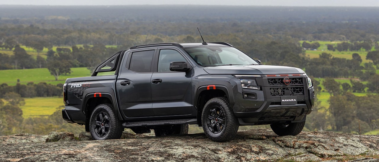 Dark grey Nissan Navara Pro-4X on rocky granite hilltop with lush green pastoral land and gum trees behind.