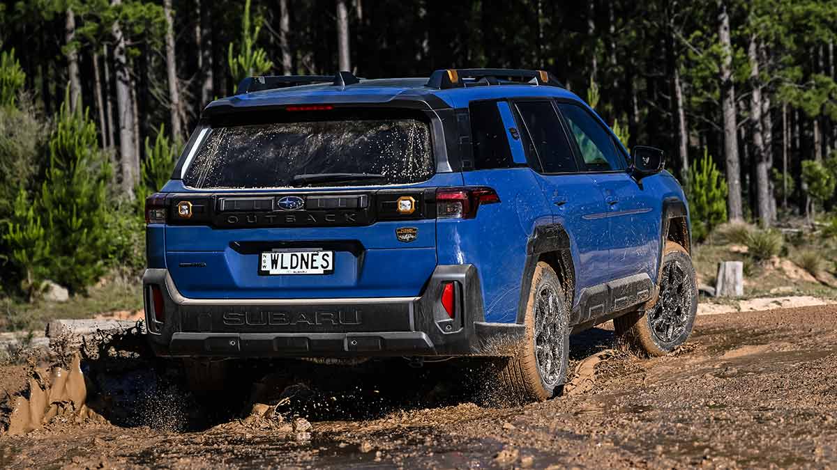 Rear view of blue Subaru Outback Wilderness driving through mud on dirt trail in Australian plantation forest.