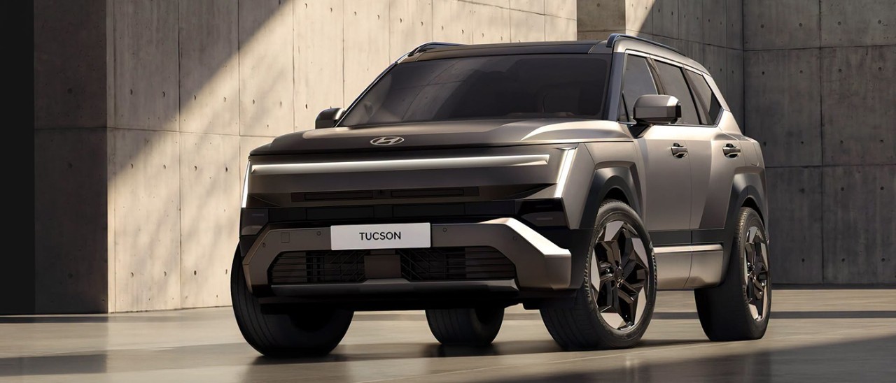 Grey metallic Hyundai Tucson SUV surrounded by large concrete walls with shafts of light across vehicle and building.