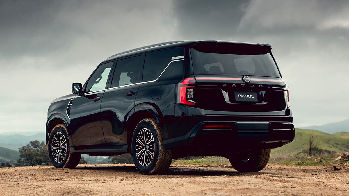 The rear of a black Y63 Nissan Patrol 2027, parked outside on a gravel road against a grey sky background  