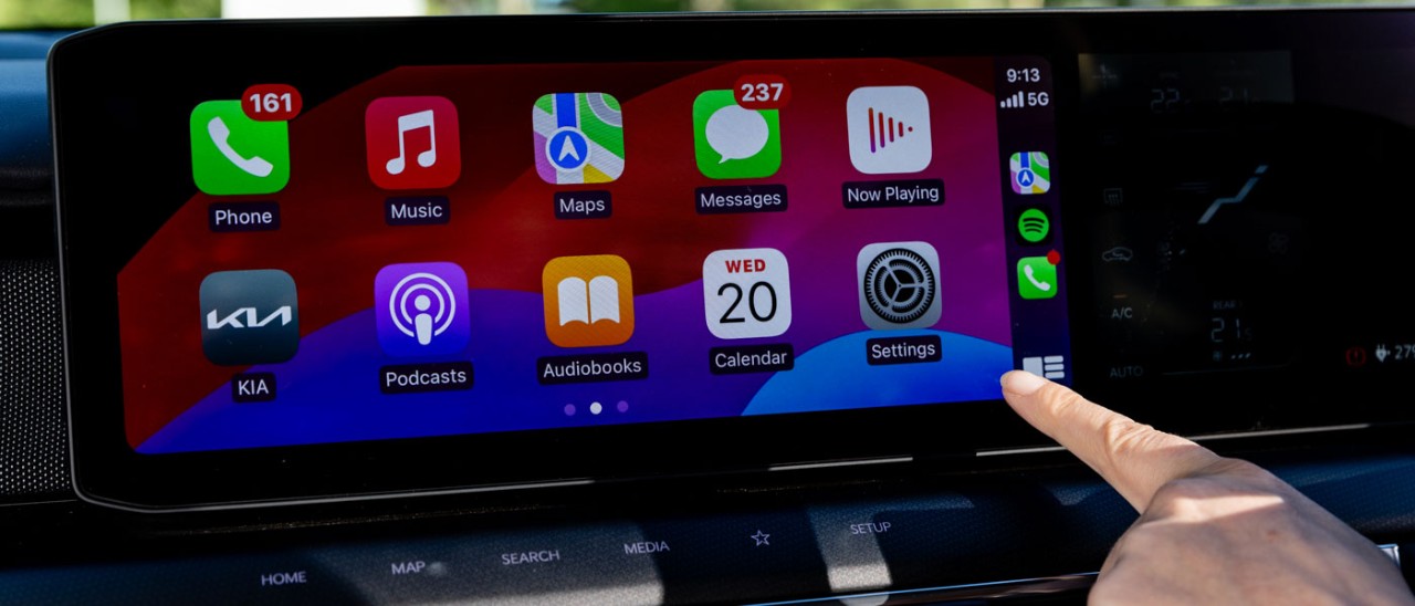 Apple CarPlay A hand pointing to a car infotainment display showing Apple CarPlay