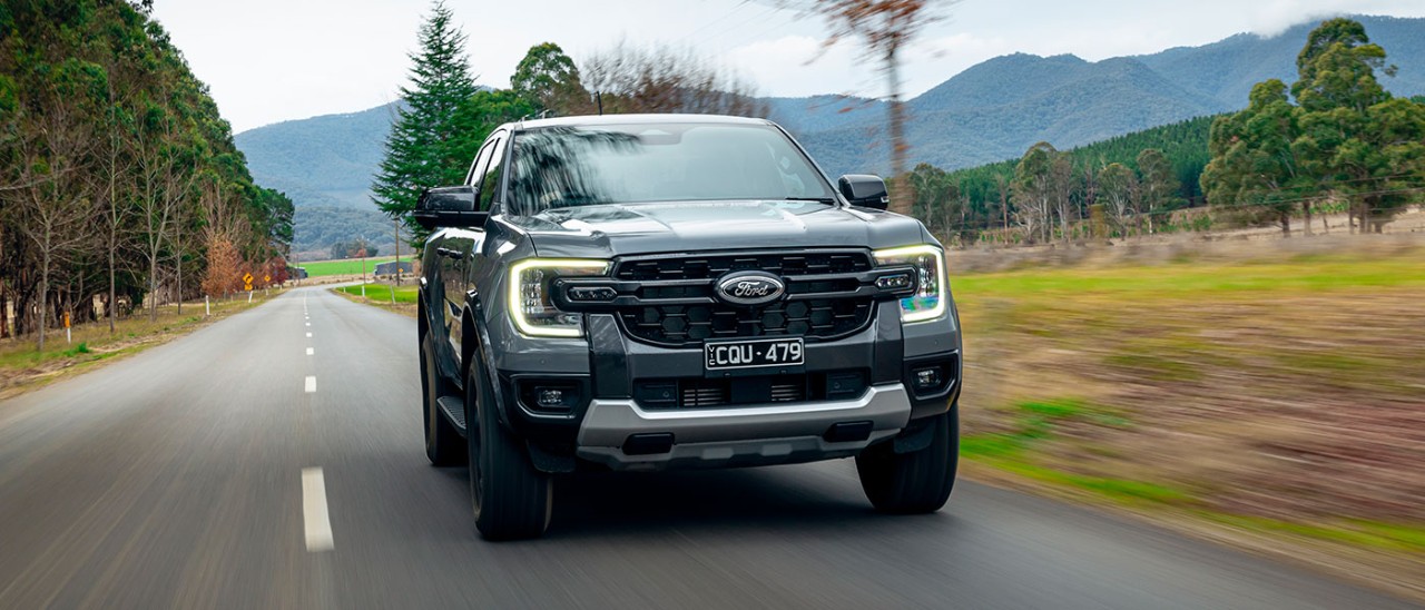 Metallic grey Ford Ranger Tremor dual-cab ute on rural tree-lined bitumen road with high country behind