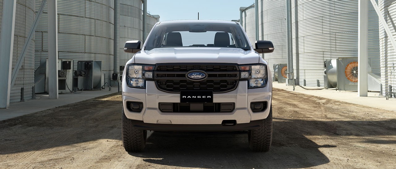 Full-frontal shot of white Ford Ranger Black Edition dual cab ute on dirt road in between two rows of large steel silos.
