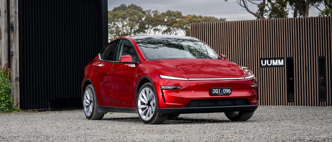 Red Tesla Model Y SUV parked in front of Mt Macedon winery building with black steel door and tall wooden screen.