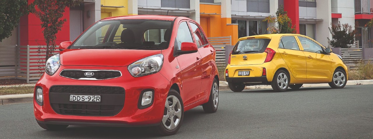red and a yellow kia picanto parked outside of townhouses on street