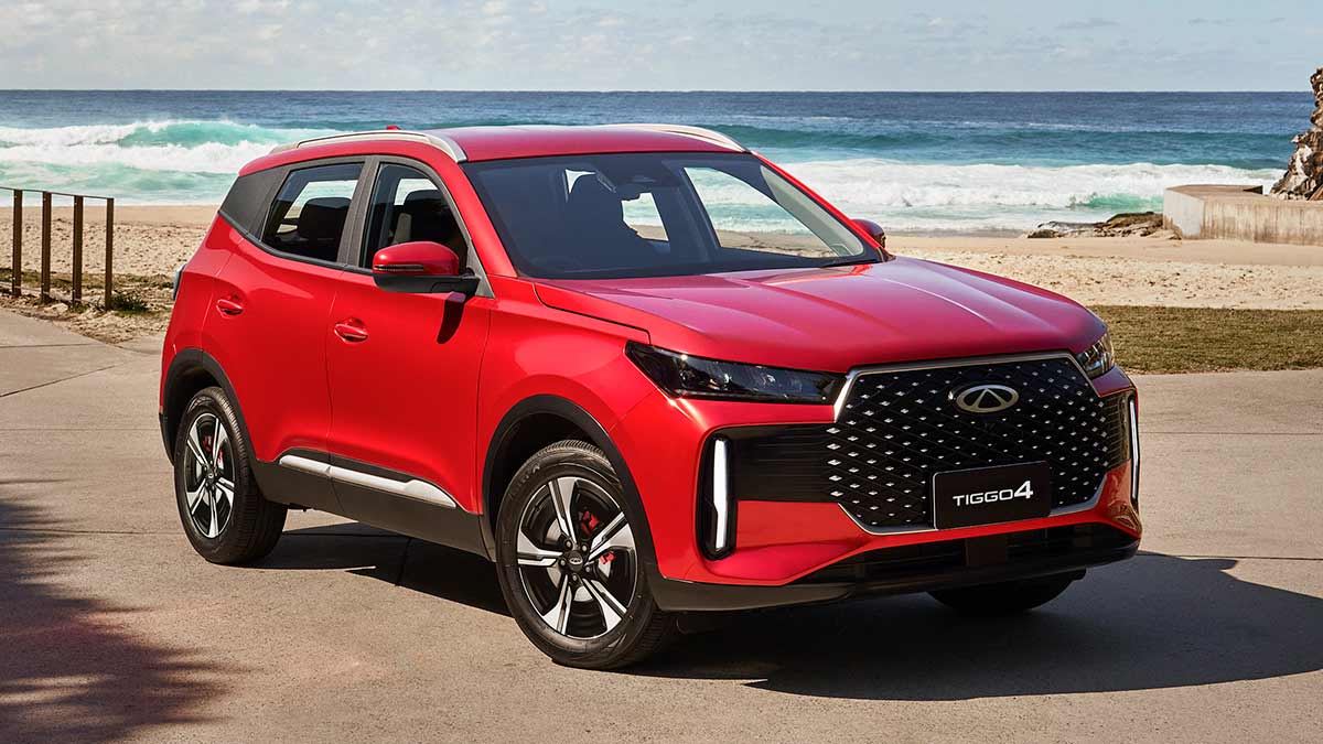 Red Chery Tiggo 4 compact SUV parked in front of beach with ocean waves breaking on shore behind