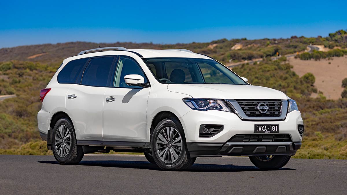 White 2019 Nissan Pathfinder large family SUV at beachside carpark with dunes behind.