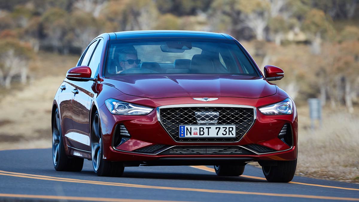 Red 2019 Genesis G70 luxury sports sedan on winding Australian alpine road in dry conditions.